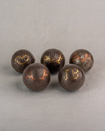 Five antique French petanque balls with textured, numbered surfaces on a plain gray fabric background. Early 20th century.