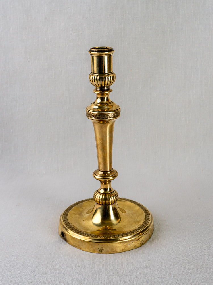 Antique French Empire palmette brass candlestick with ornate base and stem on a light background.