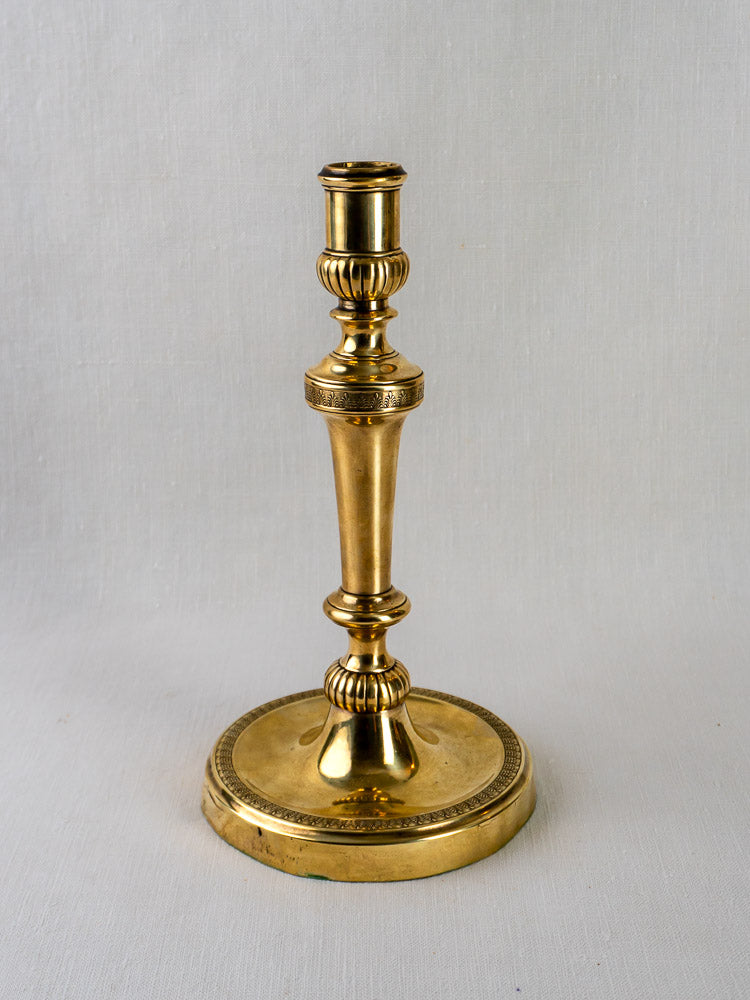 Antique French Empire Palmette brass candlestick with ornate detailing on a round base, light gray background.