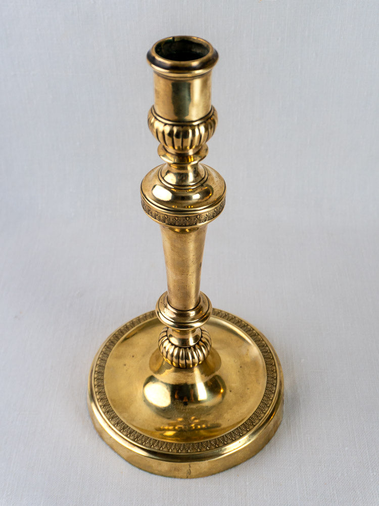 Antique French Empire palmette brass candlestick with ornate detailing on stem and base, on light gray surface.
