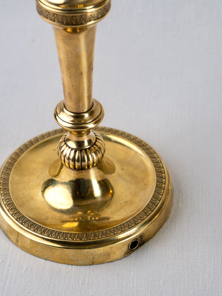 Ornate gold base of Empire Palmette Brass Candlestick with decorative edging, on white surface.