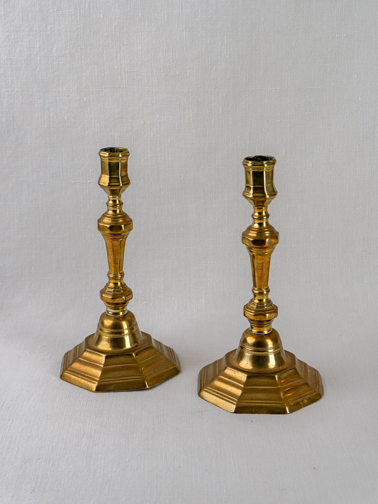 Antique French Louis XV brass candlesticks, ornate turned stems and hexagonal bases, on light gray background.