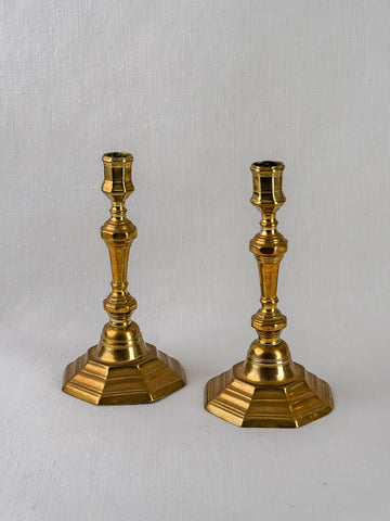Antique French Louis XV brass candlesticks, ornate turned stems and hexagonal bases, on light gray background.