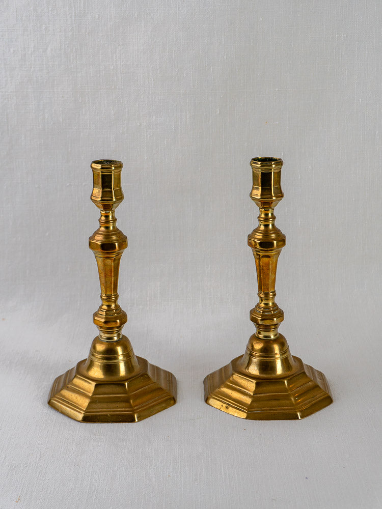 Louis XV antique French brass candlesticks with hexagonal bases and ornate stems on white textured surface.