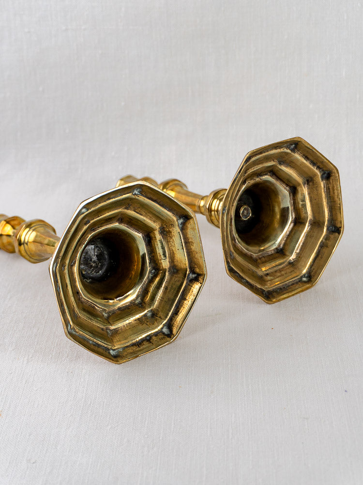 Pair of Louis XV antique French brass candlesticks showing octagonal stepped bases on white fabric.