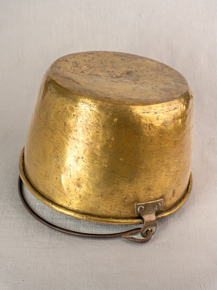 Antique French brass jam pan with hooked handle, early 19th century, displayed upside down on neutral fabric.