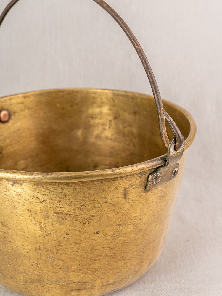 Antique French brass jam pan with tarnished surface and sturdy handle on a light fabric background.