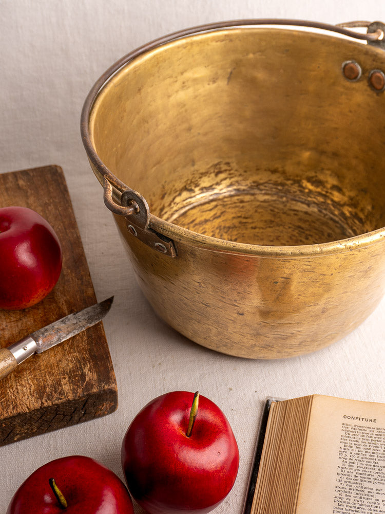 Antique French brass jam pan, early 19th century, displayed with a cutting board, knife, apples, and book.