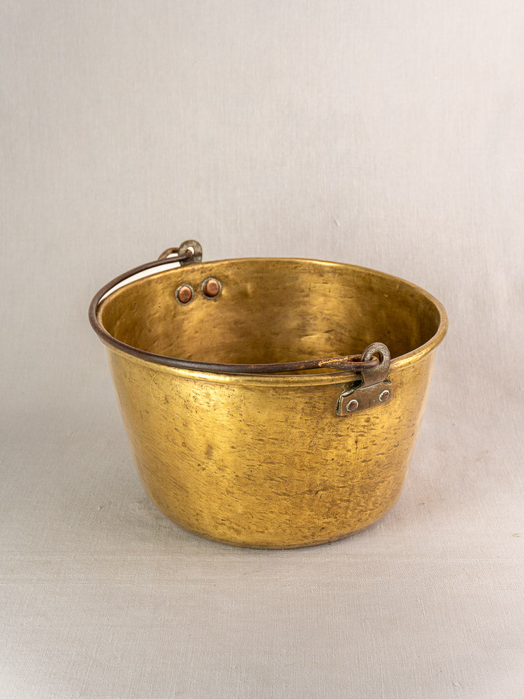 Antique French brass jam pan with round form and curved riveted handle, on a neutral surface.
