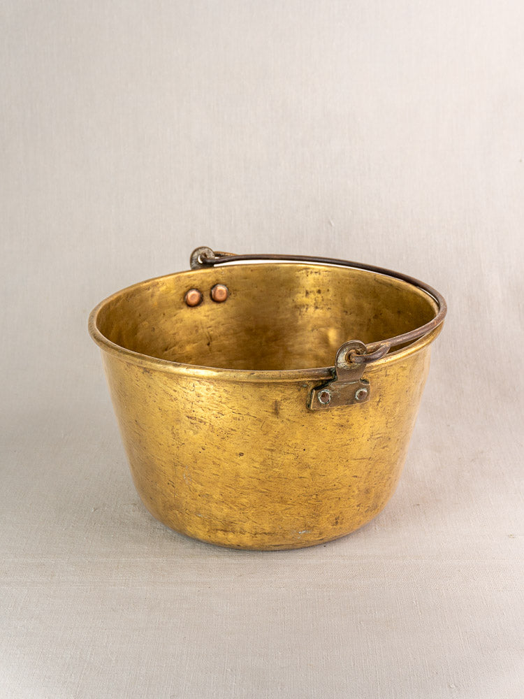 Antique French brass jam pan with curved handle, early 19th century, displayed on light fabric.