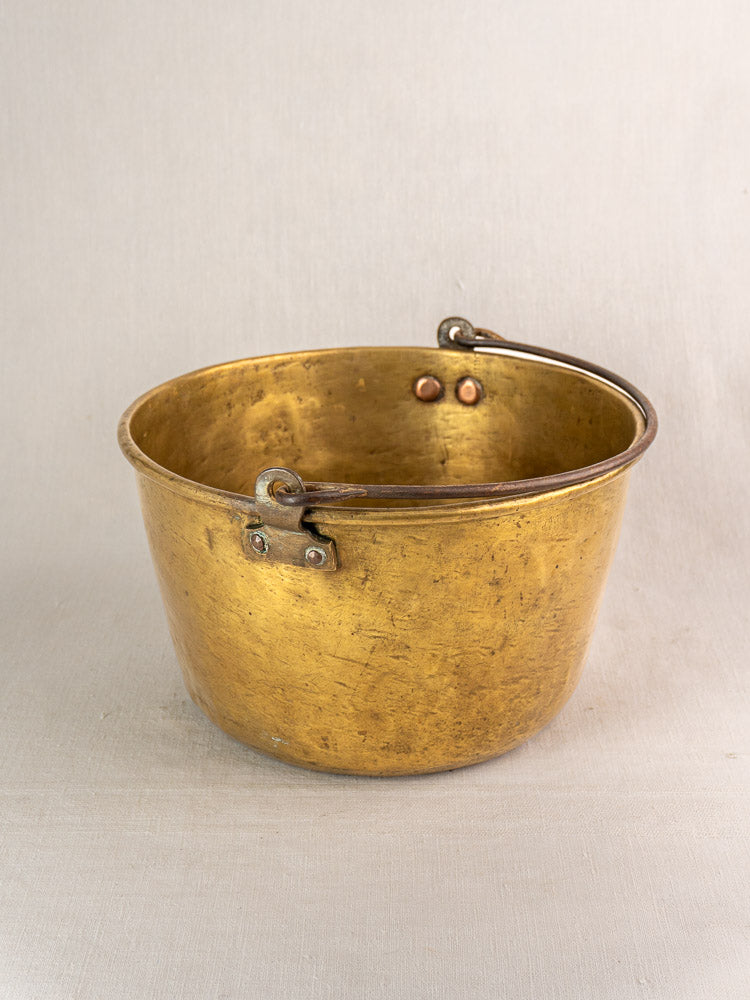Antique French brass jam pan with riveted handle displayed on a light surface against a plain background.