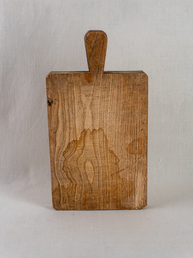 Antique French chestnut cutting board circa 1900, rectangular with handle, wood grain visible, light gray background.