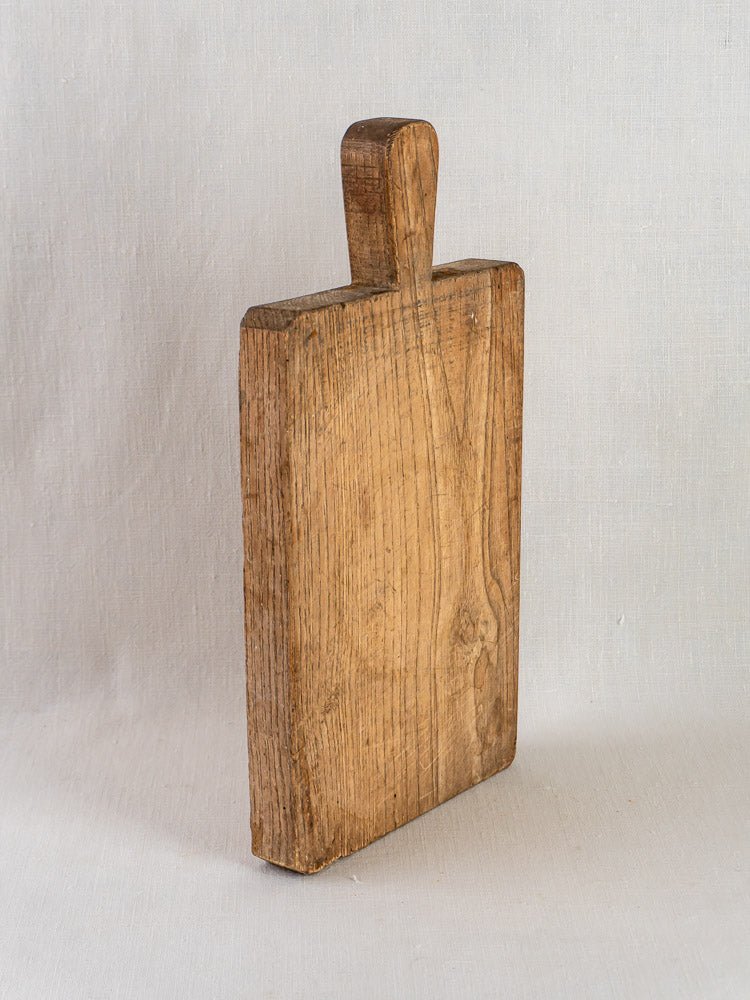 Antique French chestnut cutting board with short handle, circa 1900, upright on light surface.