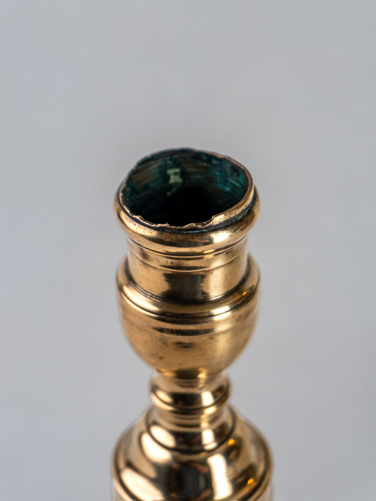 French bronze candlestick with tarnished, irregular rim and greenish residue inside, on light background.