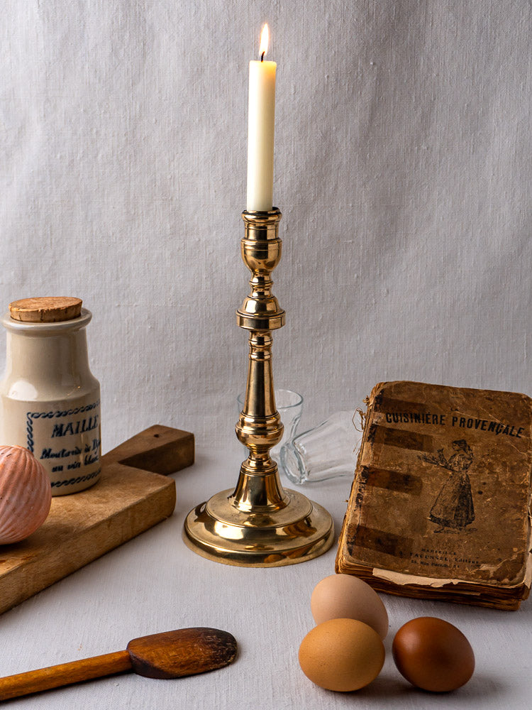 Antique French bronze candlestick with eggs, cookbook, spices, and kitchen props on wooden board.
