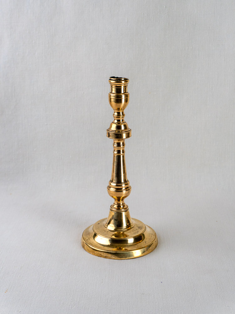 Antique French turned bronze candlestick with round base, upright on a light gray background.