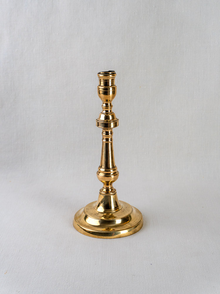 Antique French bronze candlestick with ornate baluster stem on a light surface, neutral backdrop.