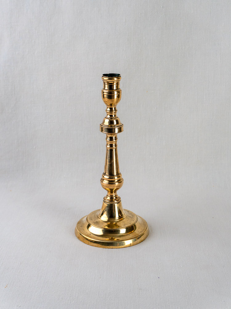 Antique French bronze candlestick with turned baluster form and round base on light gray background.