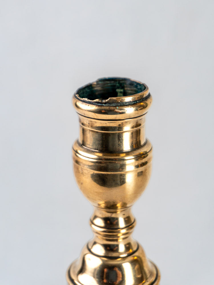 French bronze candlestick with turned baluster form, polished finish, lightly worn rim, plain light background.