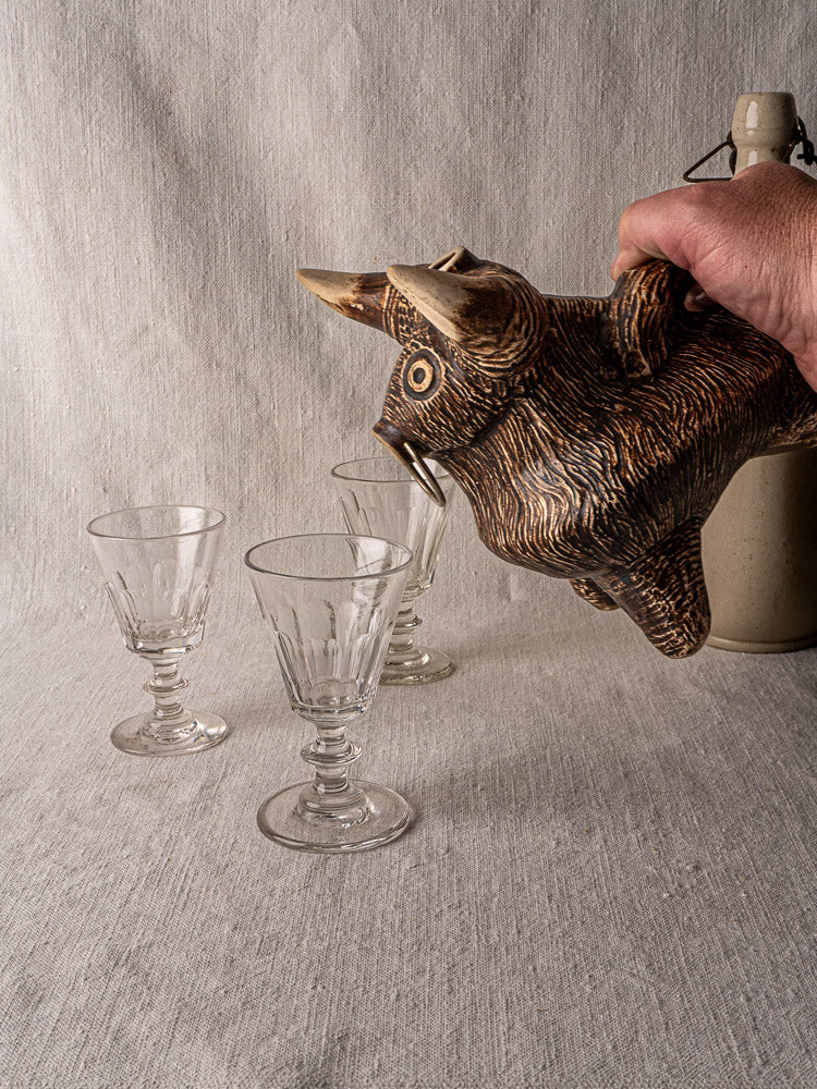 Vintage French ceramic bull pitcher, circa 1950, pouring into glass goblet on textured surface; jug in background.