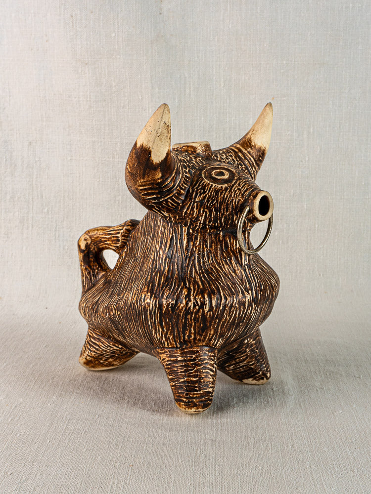 Vintage French bull zoomorphic pitcher, small textured brown ceramic with horns and nose ring, on neutral fabric background.