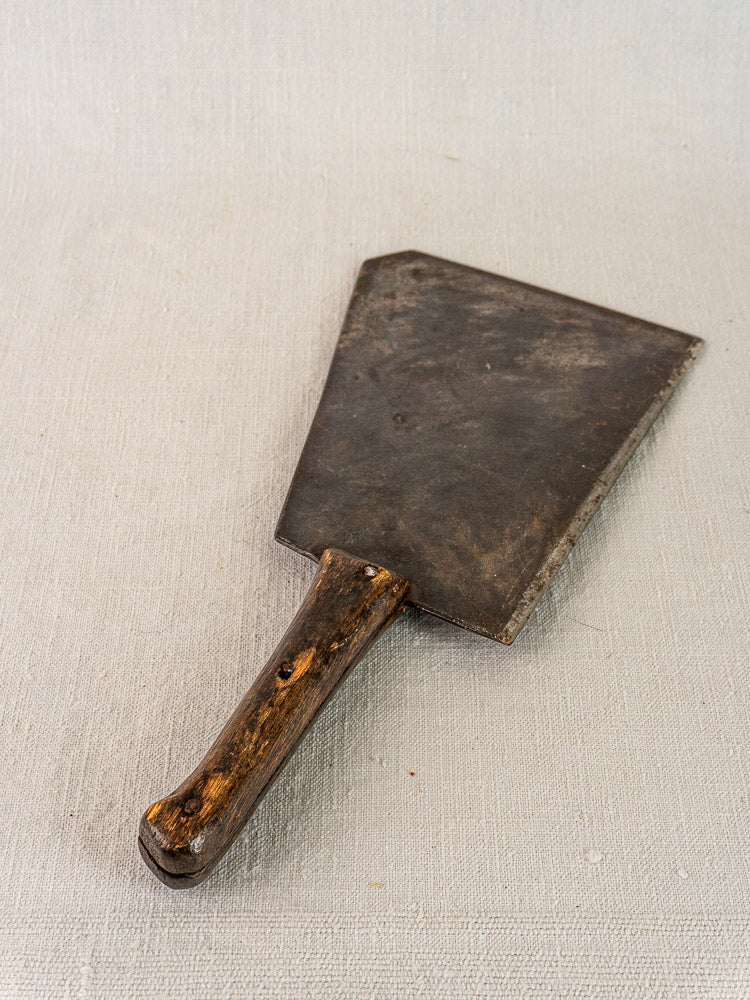 Antique French hand-forged butcher cleaver with worn wood handle and large rusted blade on textured surface.