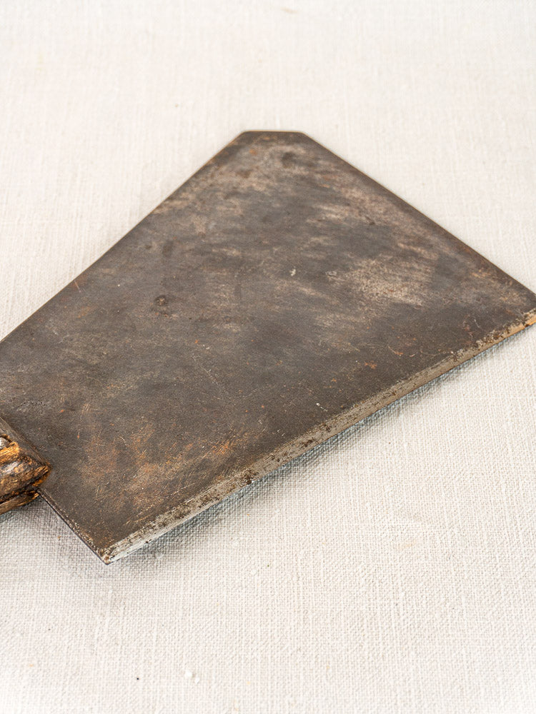 Antique French butcher cleaver with hand-forged blade and wooden handle on a light textured surface.
