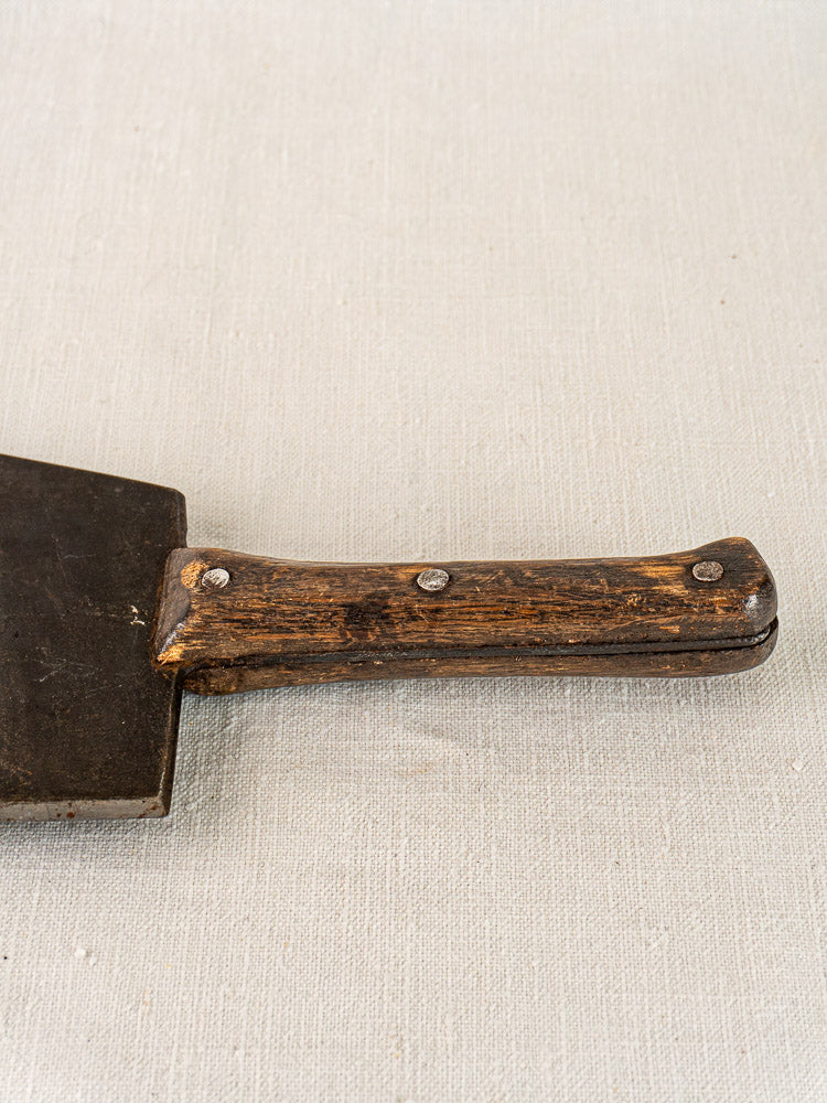 Antique French butcher cleaver, mid 19th century, hand forged with a worn wooden handle and metal rivets on light textured surface.