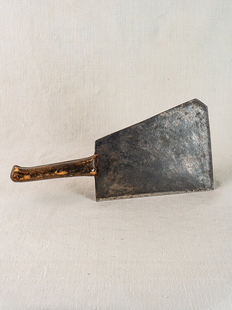 Antique French hand-forged butcher cleaver with worn wooden handle on a light textured surface.