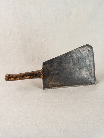 Antique French hand-forged butcher cleaver with worn wooden handle on a light textured surface.