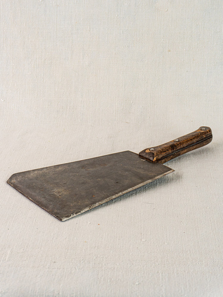 Antique French butcher cleaver, mid-19th century, hand-forged steel and worn wood handle on light textured surface.