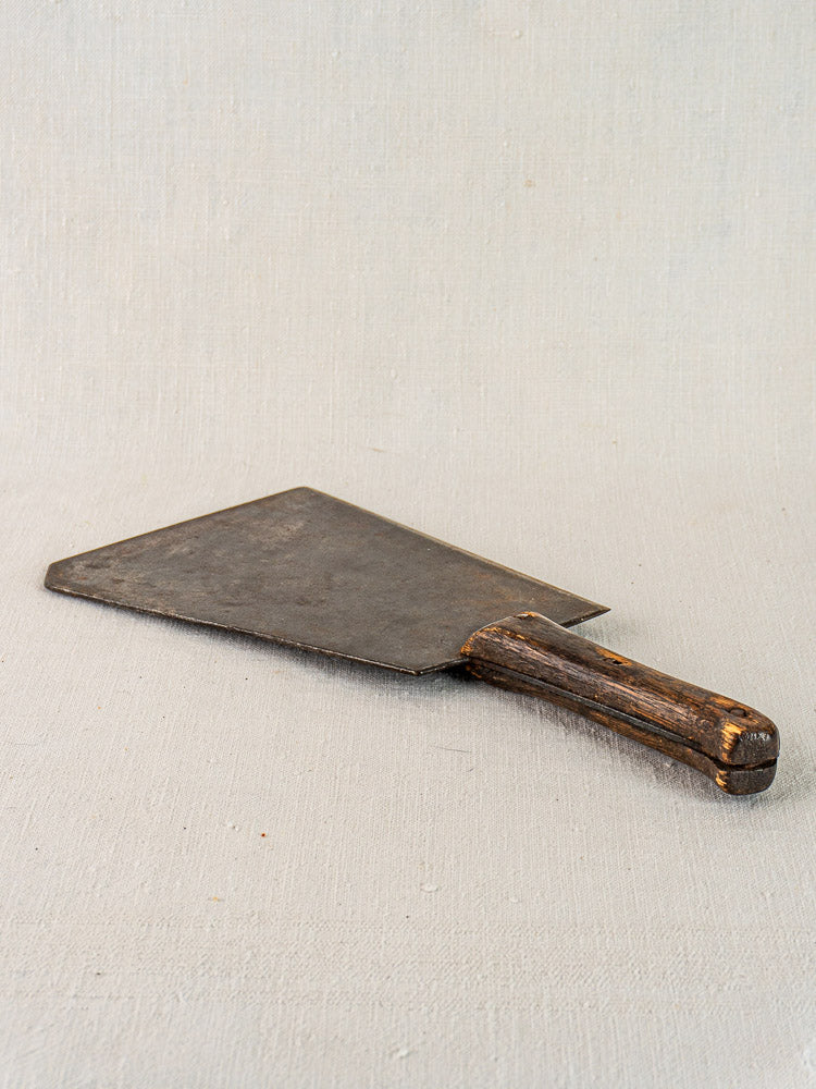 Antique French butcher cleaver with wide blade and worn wooden handle on a light textured surface.