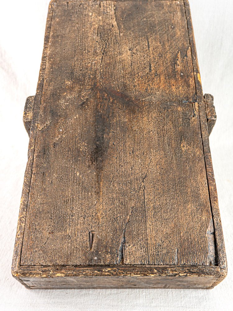 Antique French oak tool tote with hand-forged nails and weathered patina, top view on light surface.