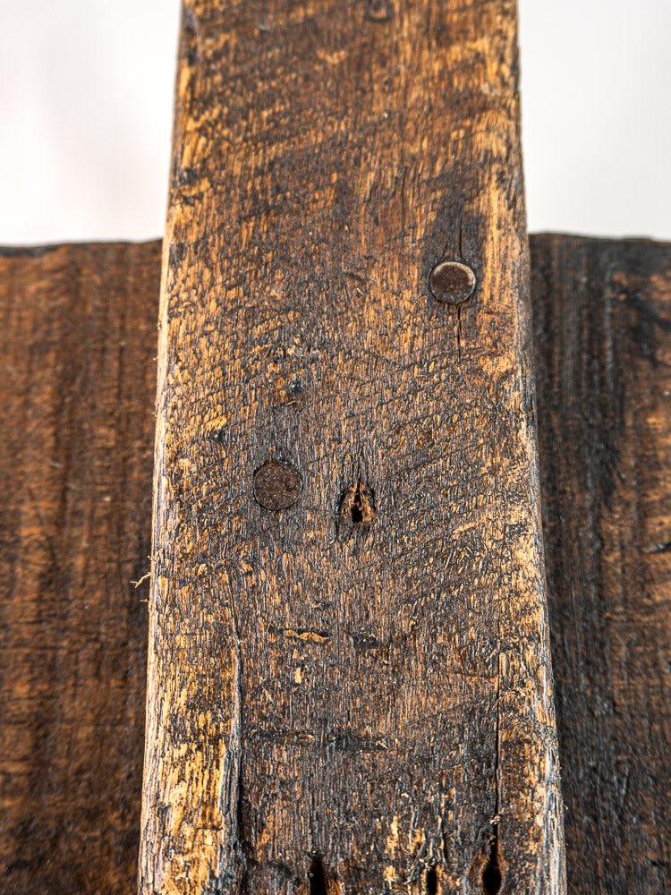 Intersecting weathered oak planks with rough grain and hand-forged rusty nails, blurred light background.