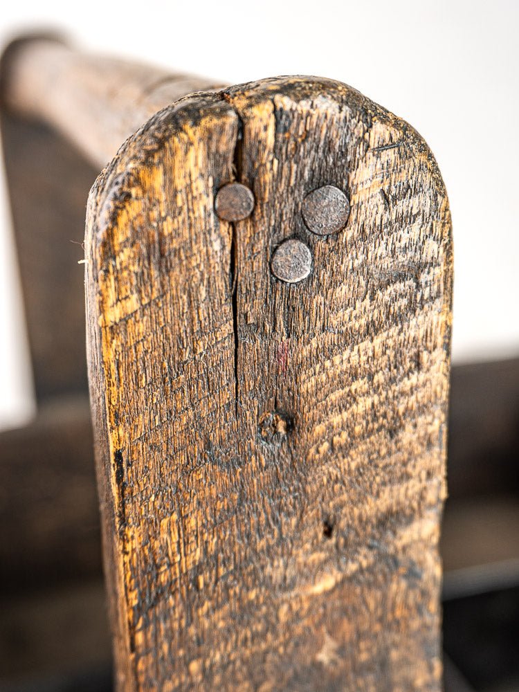 Weathered oak plank end with three round hand-forged nails, echoing antique French tool tote craftsmanship.