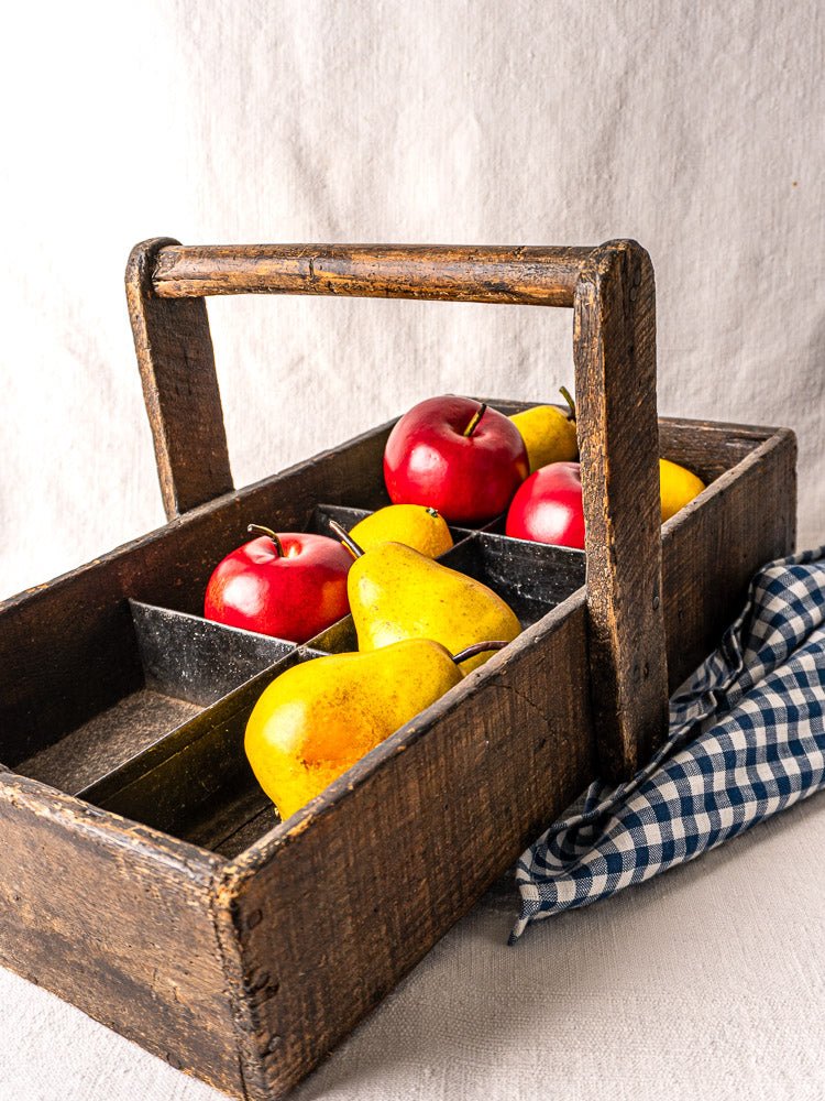 Antique French oak tool tote with hand-forged nails, holding apples and pears, on light fabric.
