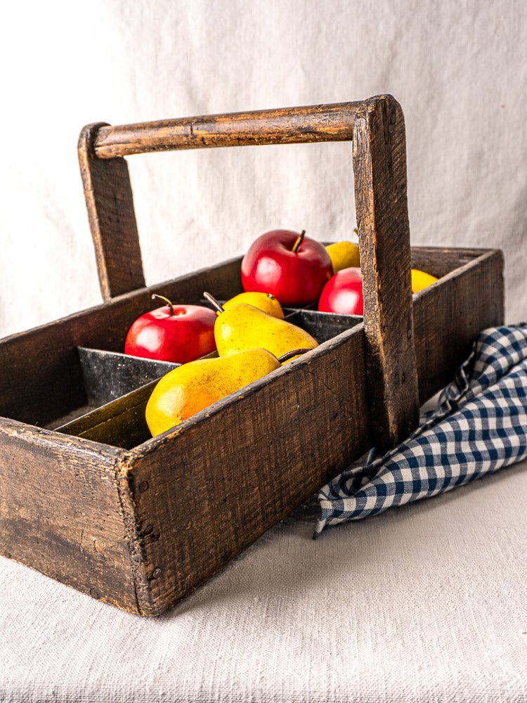 Antique French oak tool tote with hand-forged nails, sectioned and holding apples and pears.