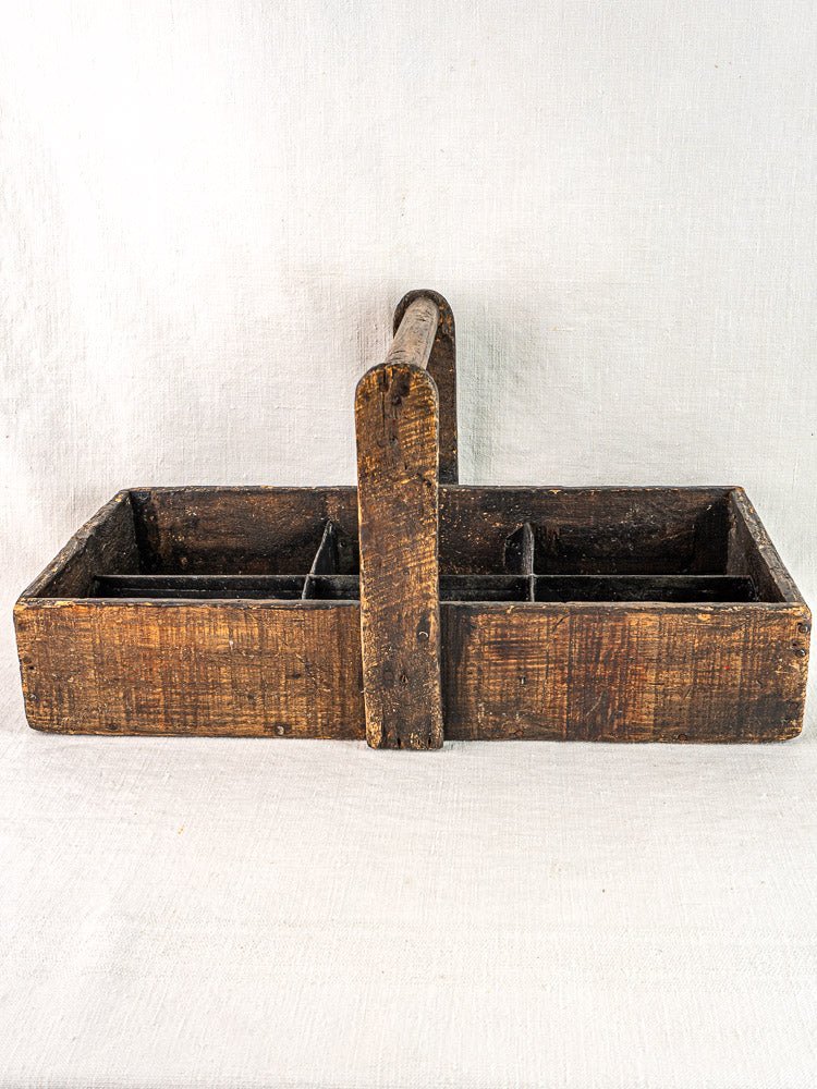 Antique French oak carpenter caddy with hand-forged nails and divided compartments on light fabric.
