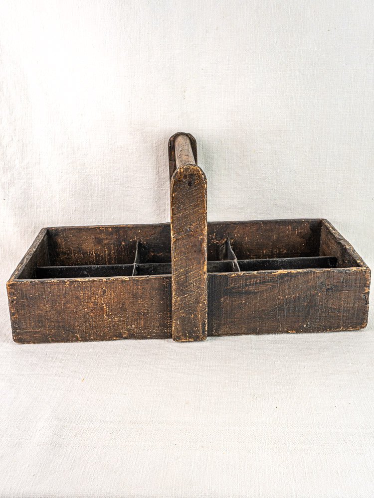 Antique French oak carpenter’s caddy with hand-forged nails and divided compartments on a light textured surface.