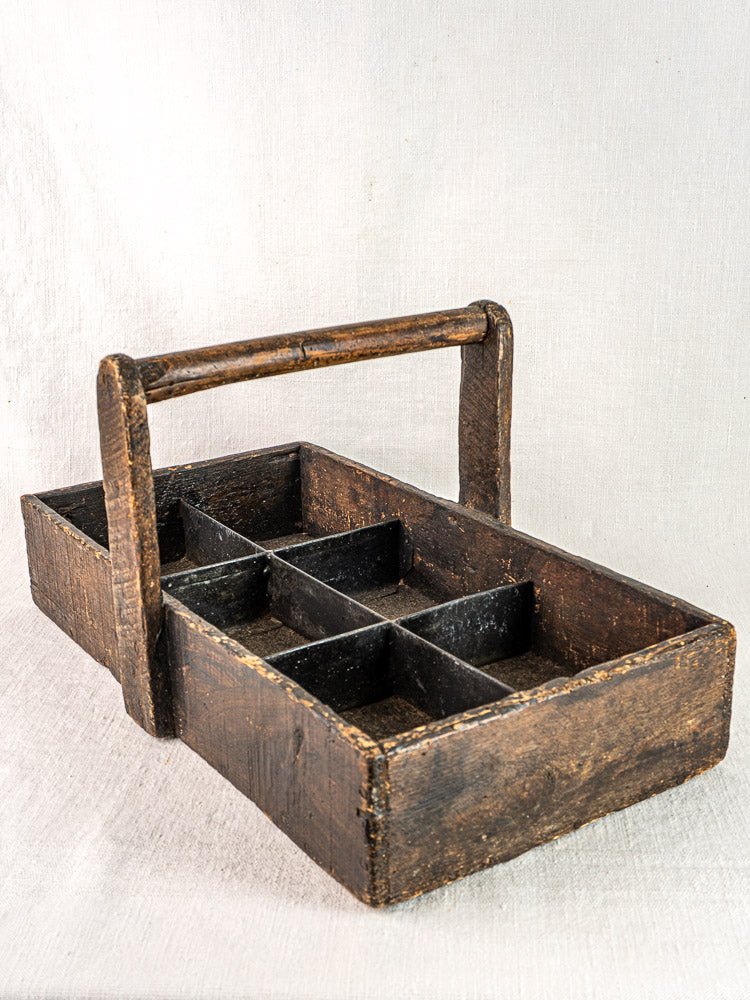 Antique French oak carpenter tote with six compartments, hand-forged nails, on light fabric background.