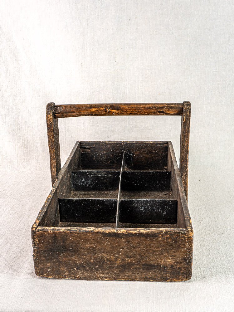 Antique French oak carpenter caddy with hand-forged nails and four compartments on light fabric background.