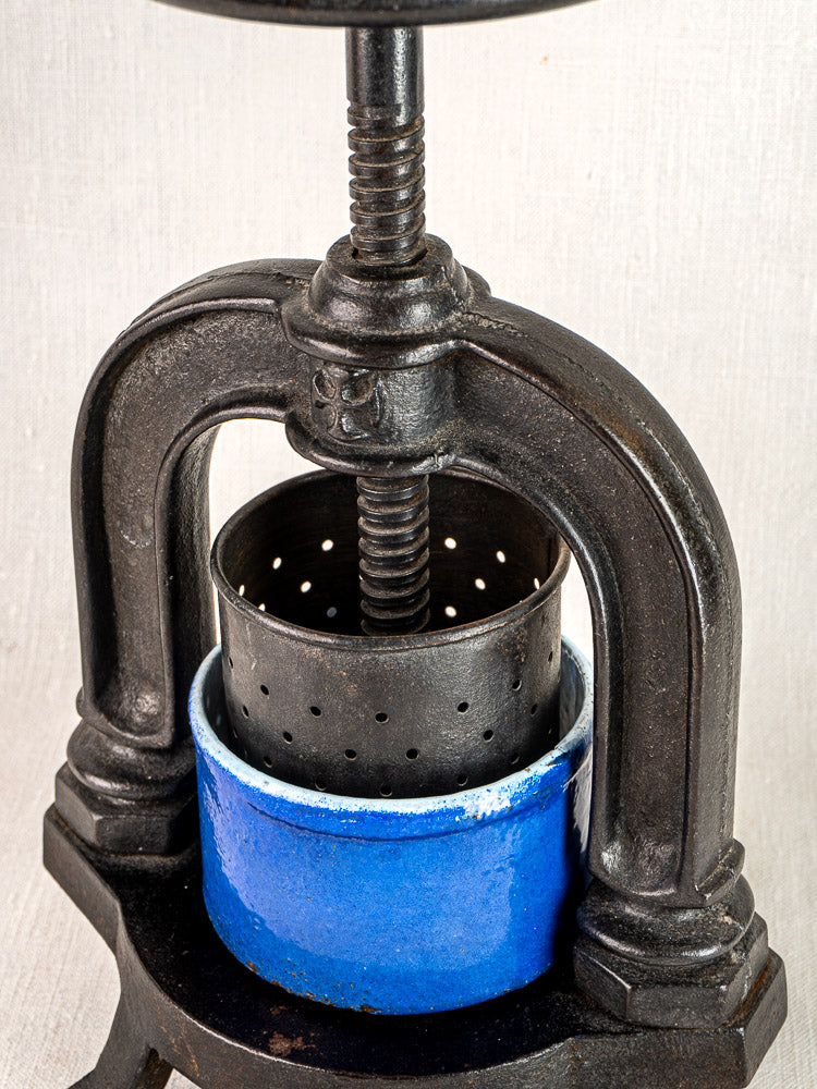 Antique French cast iron tomato press with perforated basket and blue enamel juice container.