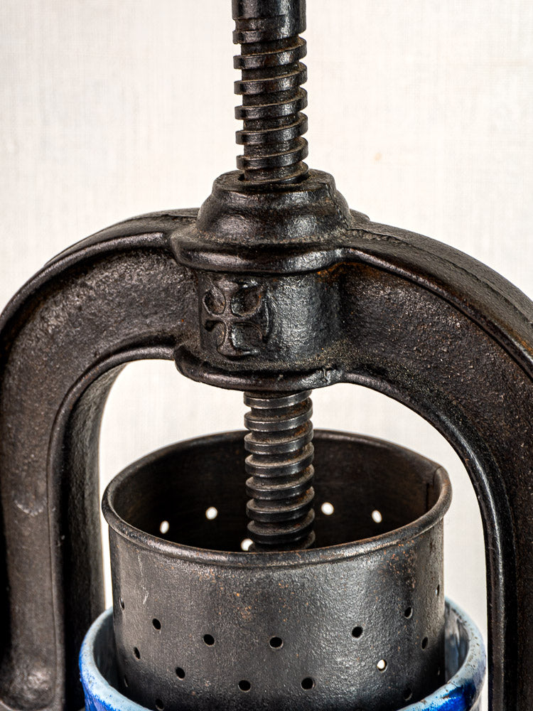 Antique French cast iron tomato press with screw mechanism and blue enamel, perforated cylindrical container.