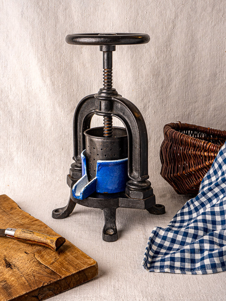 French cast iron tomato press with blue enamel and blue-lined container, styled with rustic kitchen accents.