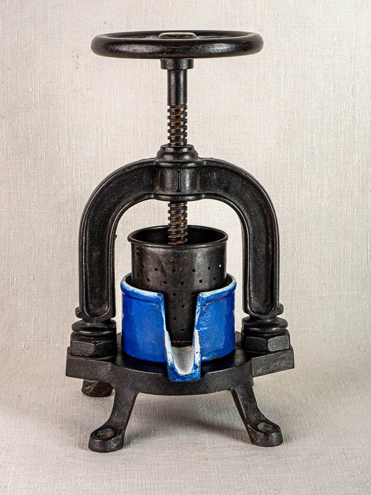 Vintage French cast iron tomato press with blue enamel, screw handle, and four legs.