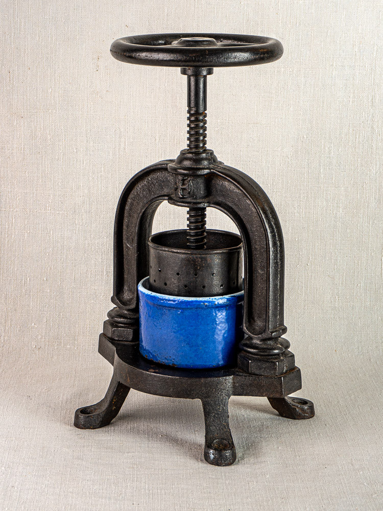 Antique French cast iron tomato press with blue enamel base and large screw handle on curved legs.