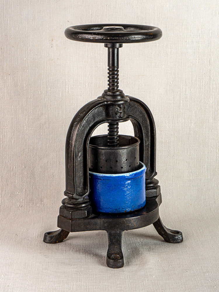 Antique French cast iron tomato press with blue enamel and classic screw mechanism, neutral background.