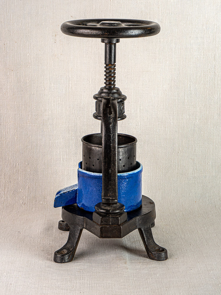 Antique French cast iron tomato press with blue enamel, crank handle, and perforated chamber.