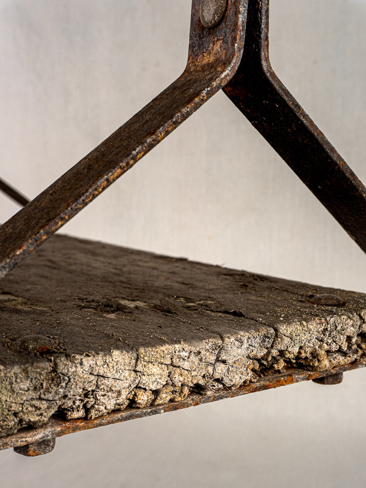 Antique French child’s swing, circa 1900, with weathered wood seat and rusted iron frame against light background.