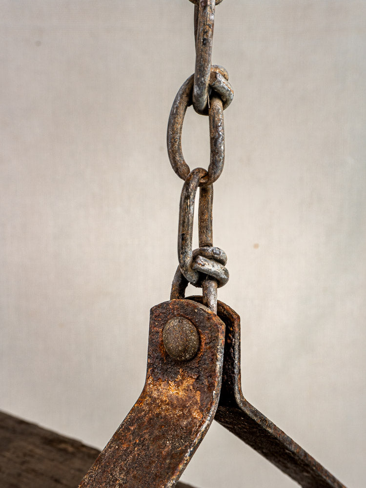 Rusty iron chain link on weathered wood and iron frame of antique French child’s swing, plain background.
